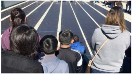 Students watch as solar cars start down the track during the Solar Car Challenge race event for middle school teams 
